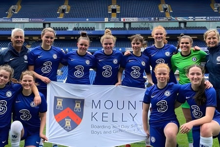 Un grupo de jugadoras de fútbol posan en el campo con una pancarta de la Mount Kelly School.