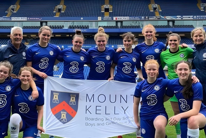 Un grupo de jugadoras de fútbol posan en el campo con una pancarta de la Mount Kelly School.