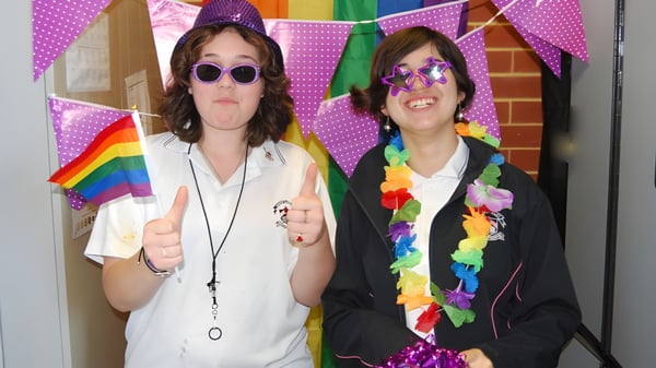 Dos alumnas de la Mount Lawley Senior High School posan frente a un fondo decorado coloridamente con banderas del arcoíris.