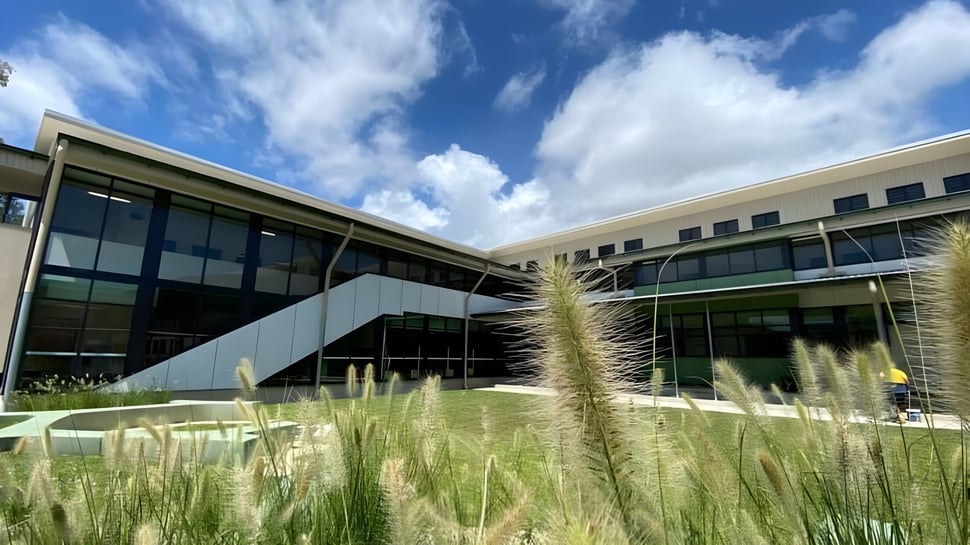 Un moderno edificio de vidrio y concreto con una superficie de césped delante en el campus de la Mount Saint Michael School bajo un cielo azul con nubes blancas.