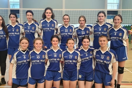 Un grupo de jóvenes jugadoras de voleibol en camisetas azules posan en el gimnasio de la Mount Saint Michael School.