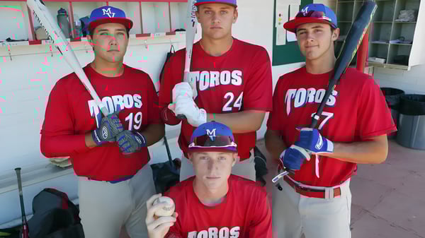 Tres estudiantes de la Mountain View High School están en uniformes de béisbol en el dugout.