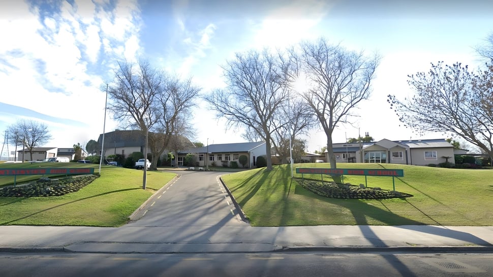 Un camino pavimentado atraviesa una superficie de césped bien cuidada con árboles desnudos en el campus de la Mountainview High School.