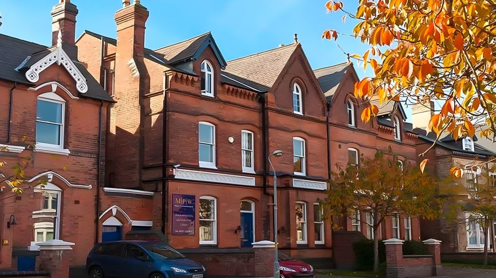 El edificio de ladrillo de varios pisos con arquitectura decorada de MPW Birmingham está rodeado de colorido follaje de otoño.