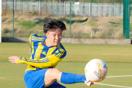 Un estudiante de MPW Birmingham juega rugby en un campo de césped rodeado de una cerca de alambre.