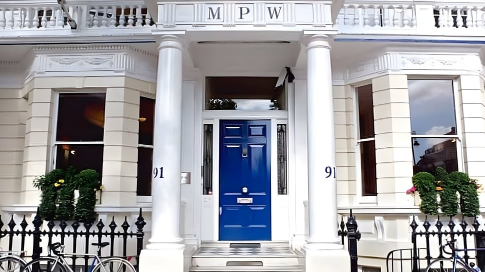 El edificio de MPW London muestra columnas blancas y una puerta de entrada azul con una valla de hierro forjado en primer plano.