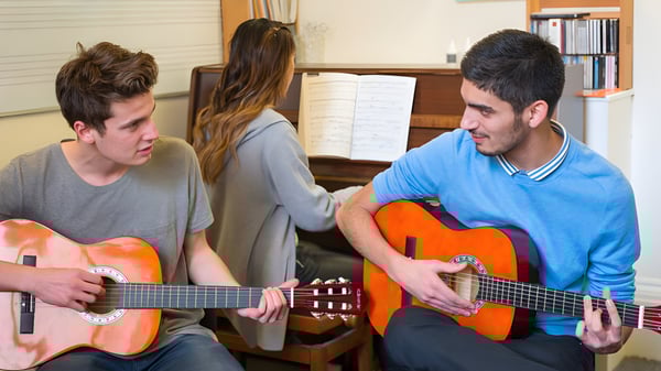 Tres estudiantes de la MPW London tocan guitarras en una sala con estanterías de libros.