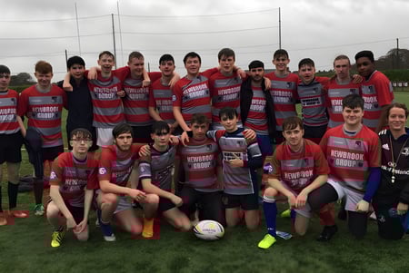 Un grupo de jóvenes futbolistas en uniformes rojos y grises posan en el campo deportivo del Mullingar Community College.