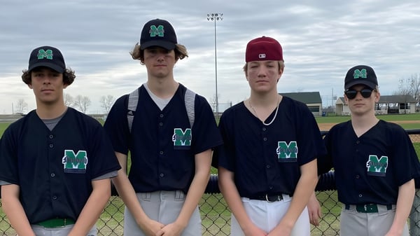 Un grupo de estudiantes que juegan al béisbol con ropa uniforme se encuentra en el campo de béisbol del Murdoch Mackay Collegiate bajo un cielo nublado.