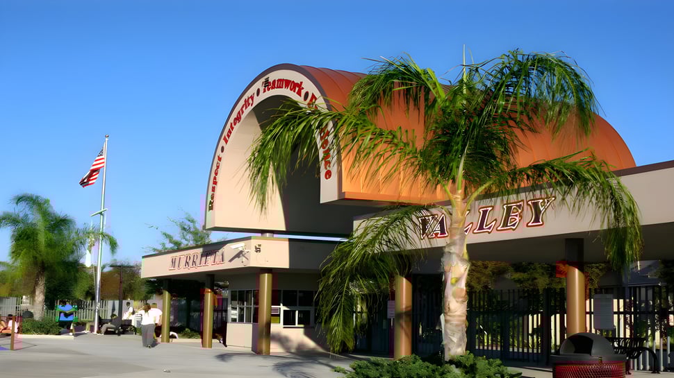 El edificio naranja con el arco distintivo en la entrada pertenece a la Murietta Valley High School y está rodeado de palmeras.