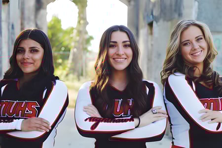 Tres alumnas de la Murietta Valley High School están frente a una pared de ladrillos y llevan camisetas deportivas iguales con la inscripción UHS.