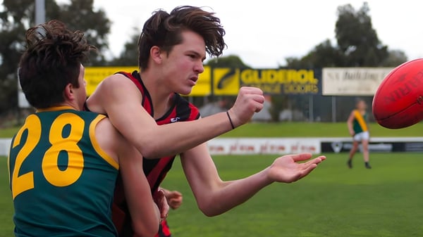 Un estudiante de la Murray Bridge High School corre con un balón de fútbol en un campo deportivo con un marcador en el fondo.