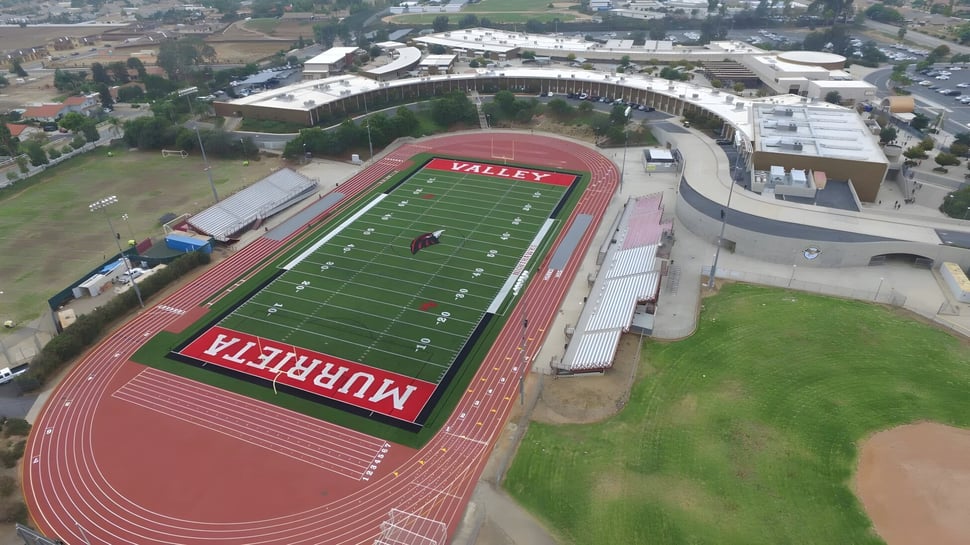 Vista aérea del gran estadio deportivo con campo de fútbol rojo y pista en el Murrieta Valley Unified School District.