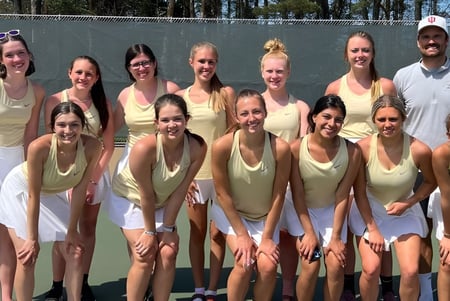 Un grupo de estudiantes de la Muskegon Catholic Central High School posan en la cancha de tenis frente a un fondo boscoso.