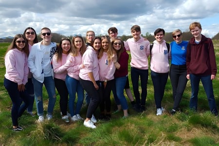 Un grupo de alumnas y alumnos está en un campo bajo un cielo nublado en el terreno de la Musselburgh Grammar School.