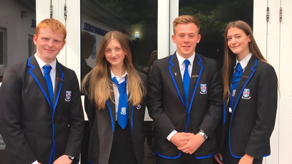 Cuatro alumnos de la Musselburgh Grammar School están en uniforme escolar frente a un edificio de noche.