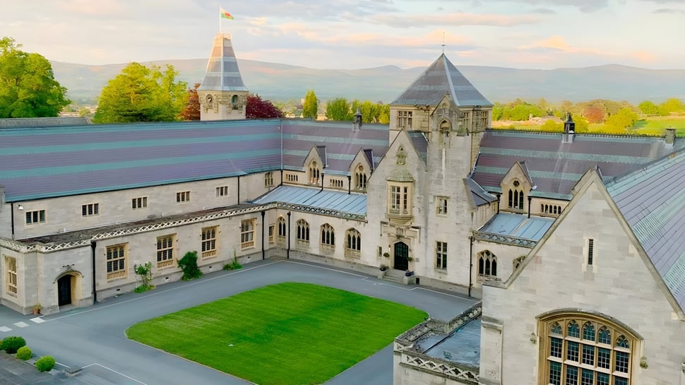 El castillo de aspecto medieval del Myddelton College con torres y un patio verde frente a un paisaje montañoso.