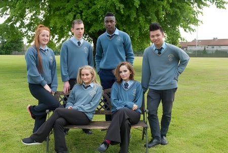 Un grupo de estudiantes en uniformes escolares posan sobre un campo de césped en el campus del Nagle Community College.