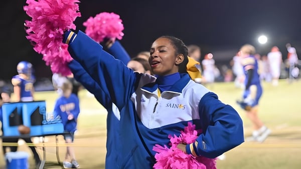 Una estudiante de la Nansemond-Suffolk Academy sostiene pompones rosas y realiza una actuación de cheerleading en el campo deportivo por la noche.