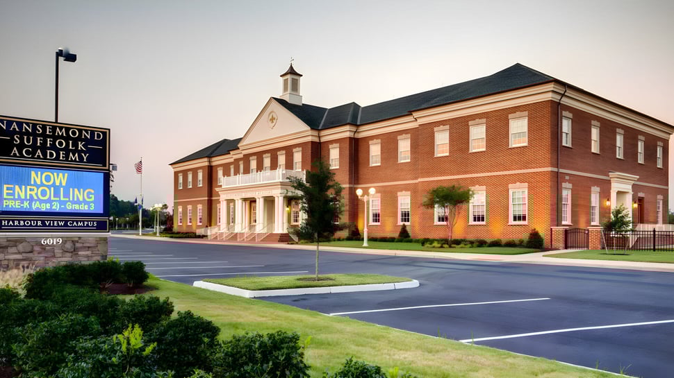 El edificio de ladrillo con torre de la Nansemond-Suffolk Academy está rodeado de un estacionamiento y áreas verdes.