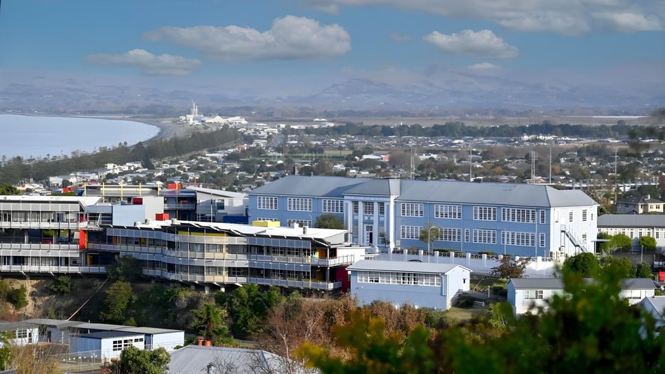 Vista de la Napier Girls' High School hacia un paisaje urbano con edificios coloridos y montañas al fondo bajo un cielo nublado.