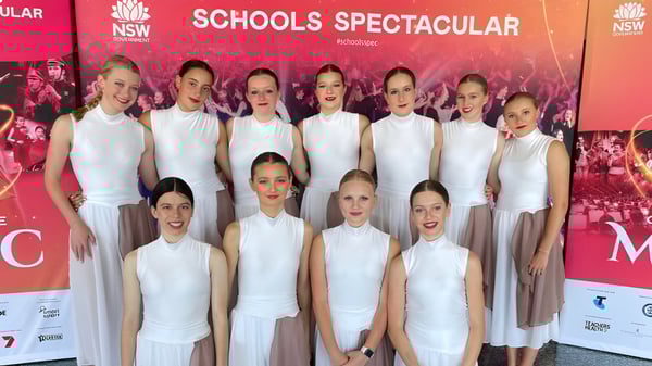 Estudiantes de la Narrabeen Sports High School posan frente a una gran pancarta roja con la inscripción Schools Spectacular en un escenario.