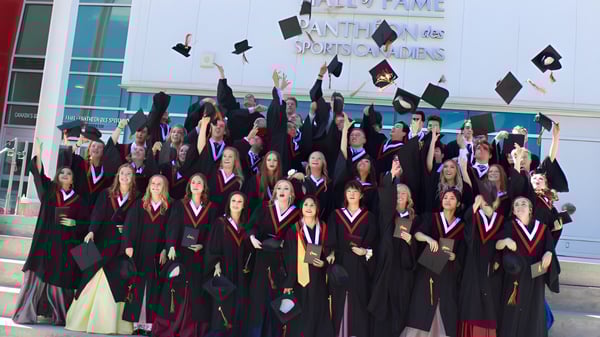 Un gran grupo de graduados de la National Sport School celebra frente a un edificio con el letrero Antho Sports Guides.