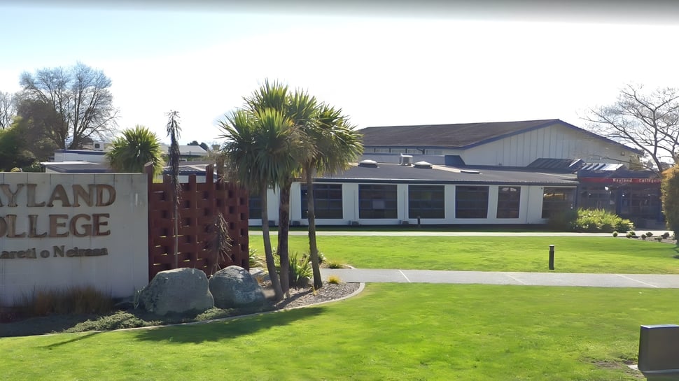 La entrada de Nayland College con un letrero y una zona verde con palmeras en primer plano.