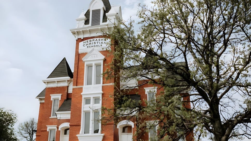 El histórico edificio de ladrillo con alto campanario en el campus de Nebraska Christian Schools está rodeado de árboles desnudos.