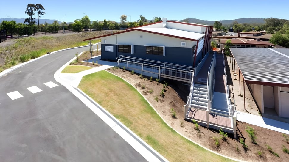 El moderno edificio de dos pisos de la Nerang State High School se encuentra en una colina cubierta de hierba con montañas al fondo.