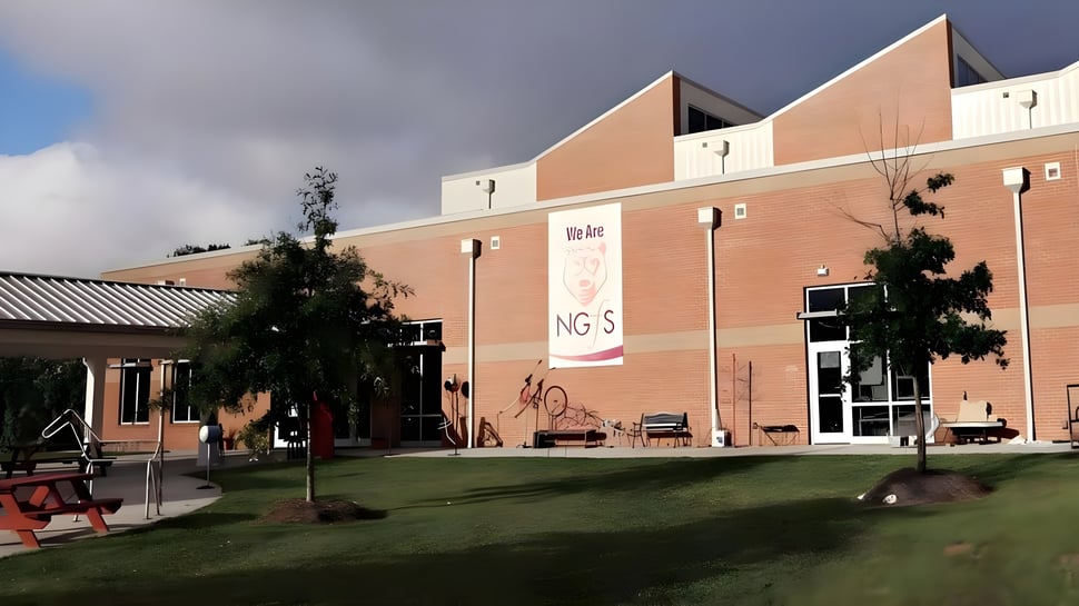 El edificio naranja de la New Garden Friends School está frente a un campo con bancos y árboles.