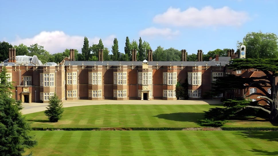 El histórico edificio de ladrillo de la New Hall School con ventanas de arco y césped cuidado en primer plano.