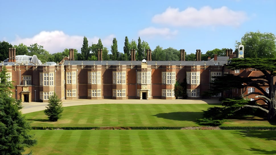 El magnífico edificio de ladrillo de la New Hall School con grandes ventanas de arco y un césped bien cuidado en el primer plano.