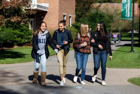 Cuatro estudiantes caminan juntos por un camino pavimentado en el campus de la New Hampton School.