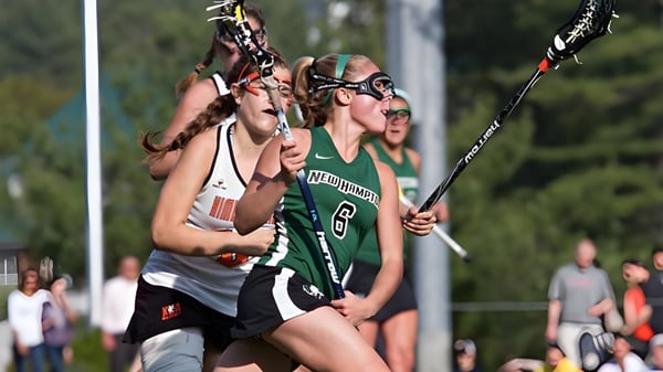 Dos jugadoras de lacrosse de la New Hampton School compiten en un campo deportivo frente a espectadores.
