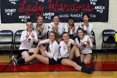 Un grupo de jóvenes atletas posan en la cancha de baloncesto de la New Hope Christian School frente a una pancarta con el nombre del equipo.