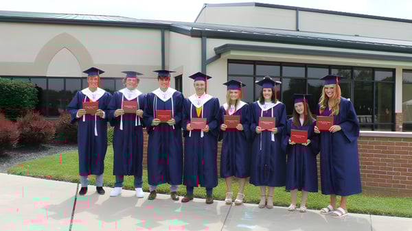 Un grupo de graduados de la New Hope Christian School está frente a un edificio de ladrillo con techo puntiagudo.