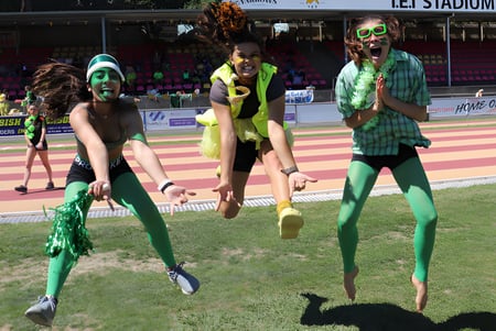 Estudiantes de la New Plymouth Girls’ High School posan con coloridos disfraces en un campo deportivo frente al estadio.
