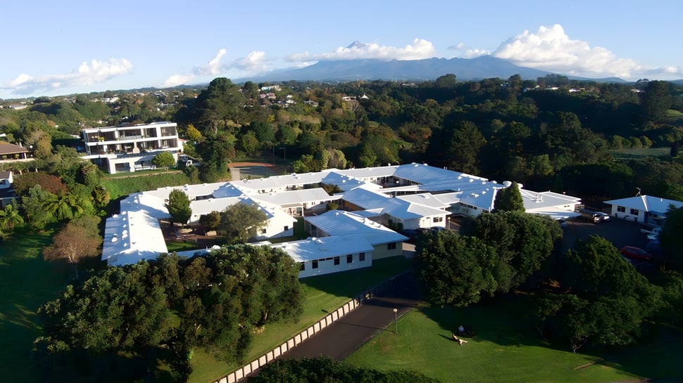 La zona exterior de la New Plymouth Girls’ High School muestra una amplia área residencial con un entorno verde y montañas al fondo.