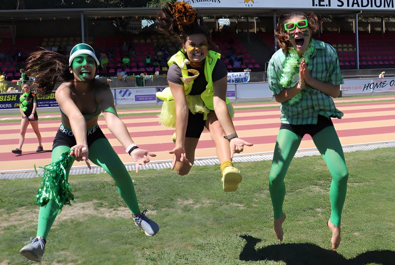 Un grupo de alumnas de la New Plymouth Girls’ High School está en coloridos disfraces en un campo deportivo con un estadio al fondo.