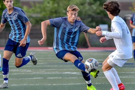 Estudiantes de la New Westminster Secondary School juegan un partido de fútbol en un campo verde.