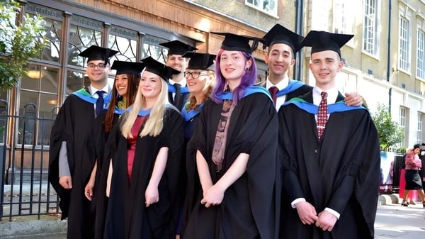 Un grupo de graduados está frente a un edificio de ladrillo en el campus de la New Westminster Secondary School.