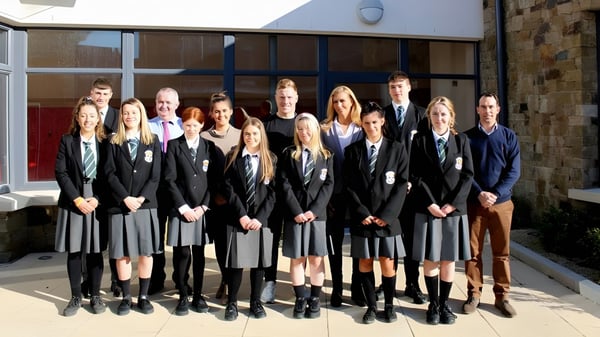 Un grupo de estudiantes del Newbridge College en traje de graduación está frente a un edificio.