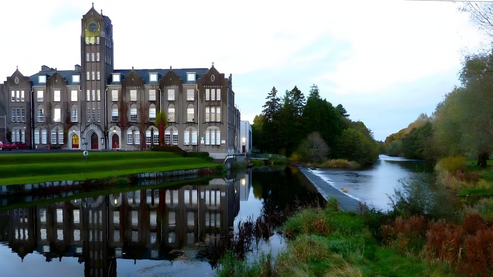 El edificio histórico del Newbridge College con un alto reloj torre se refleja en las tranquilas aguas de un canal.