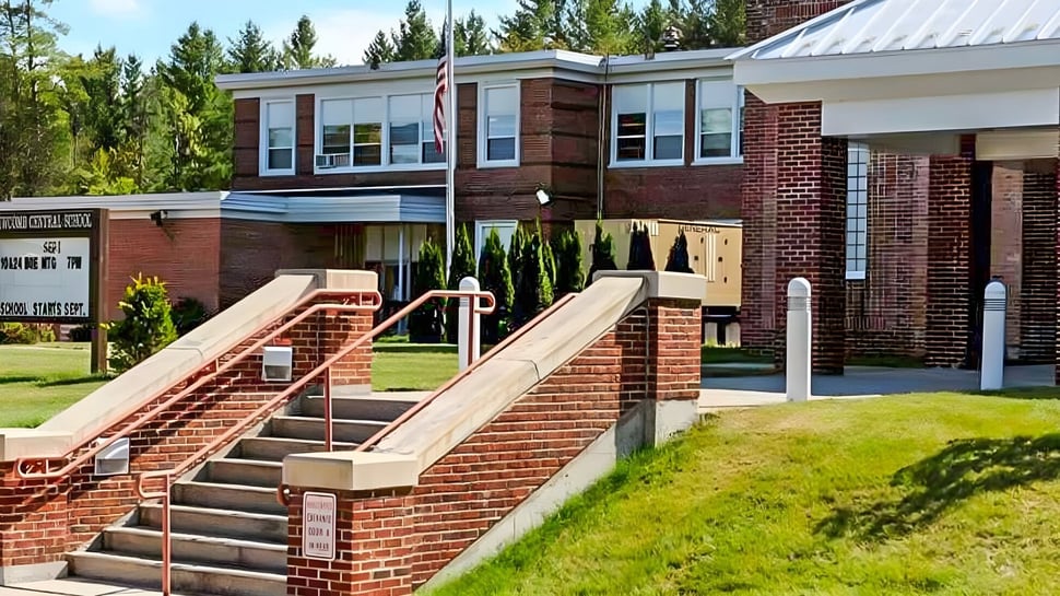 La entrada principal del edificio de ladrillo en el terreno del Newcomb Central School District con escaleras y vegetación circundante.