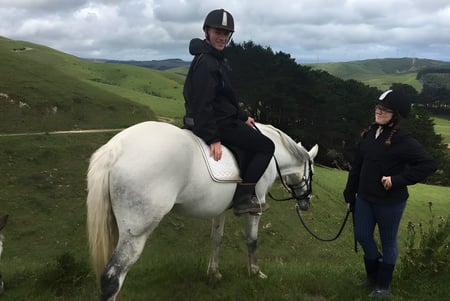 Una persona monta un caballo blanco en un prado ondulado en el terreno del Newlands College.