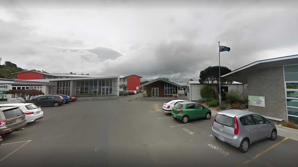 Una pequeña calle de la ciudad con edificios rojos y coches aparcados bajo un cielo nublado cerca de Newlands College.