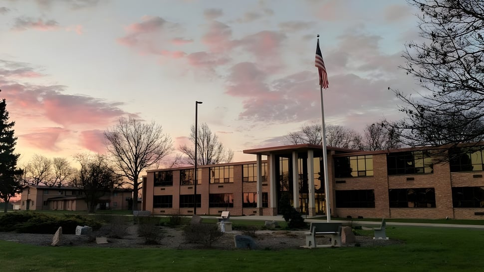 El edificio de ladrillo de varios pisos de la Newman Central Catholic High School frente a un colorido atardecer con árboles en primer plano.