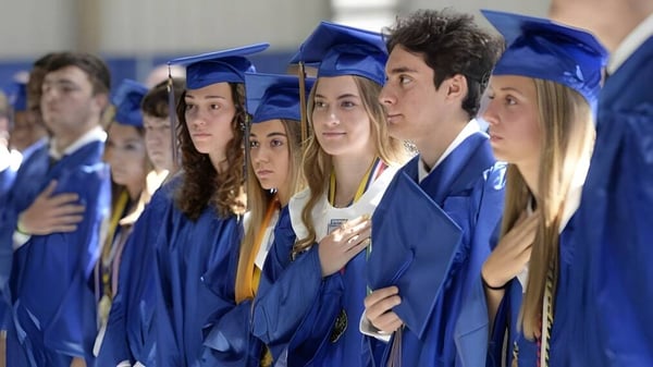 Un grupo de graduadas y graduados en togas azules está en la foto de graduación de la Newman Central Catholic High School.