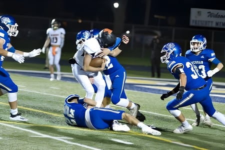Jugadores de la Newman Central Catholic High School se ven durante un partido de fútbol americano en un tackle en el campo.
